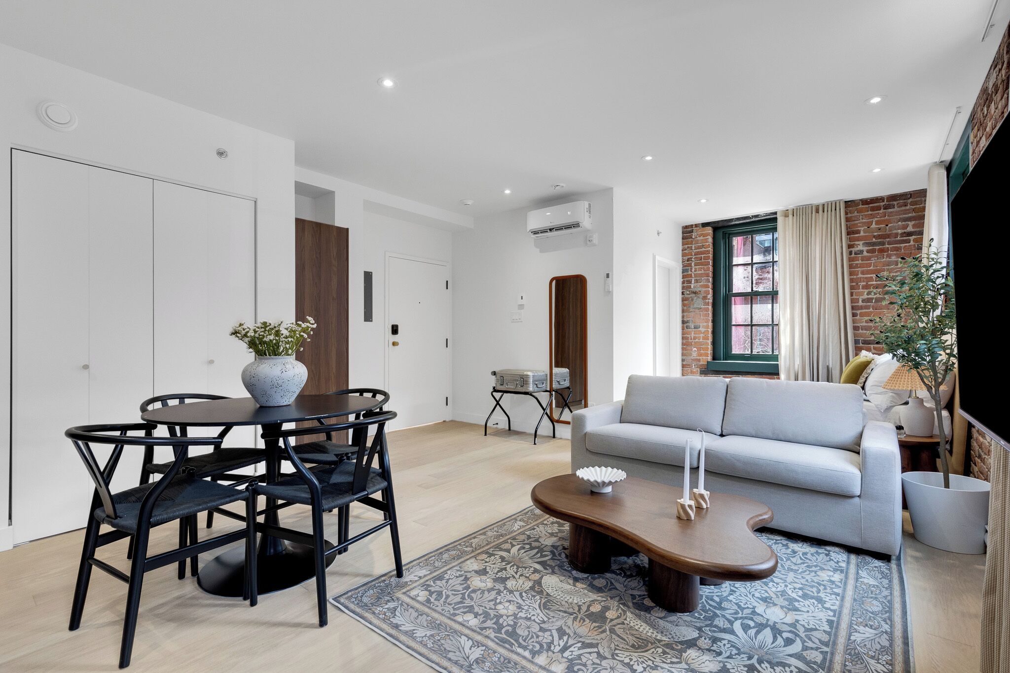 A modern living room with a grey sofa, a wooden coffee table, and a dining area with a round table and chairs.