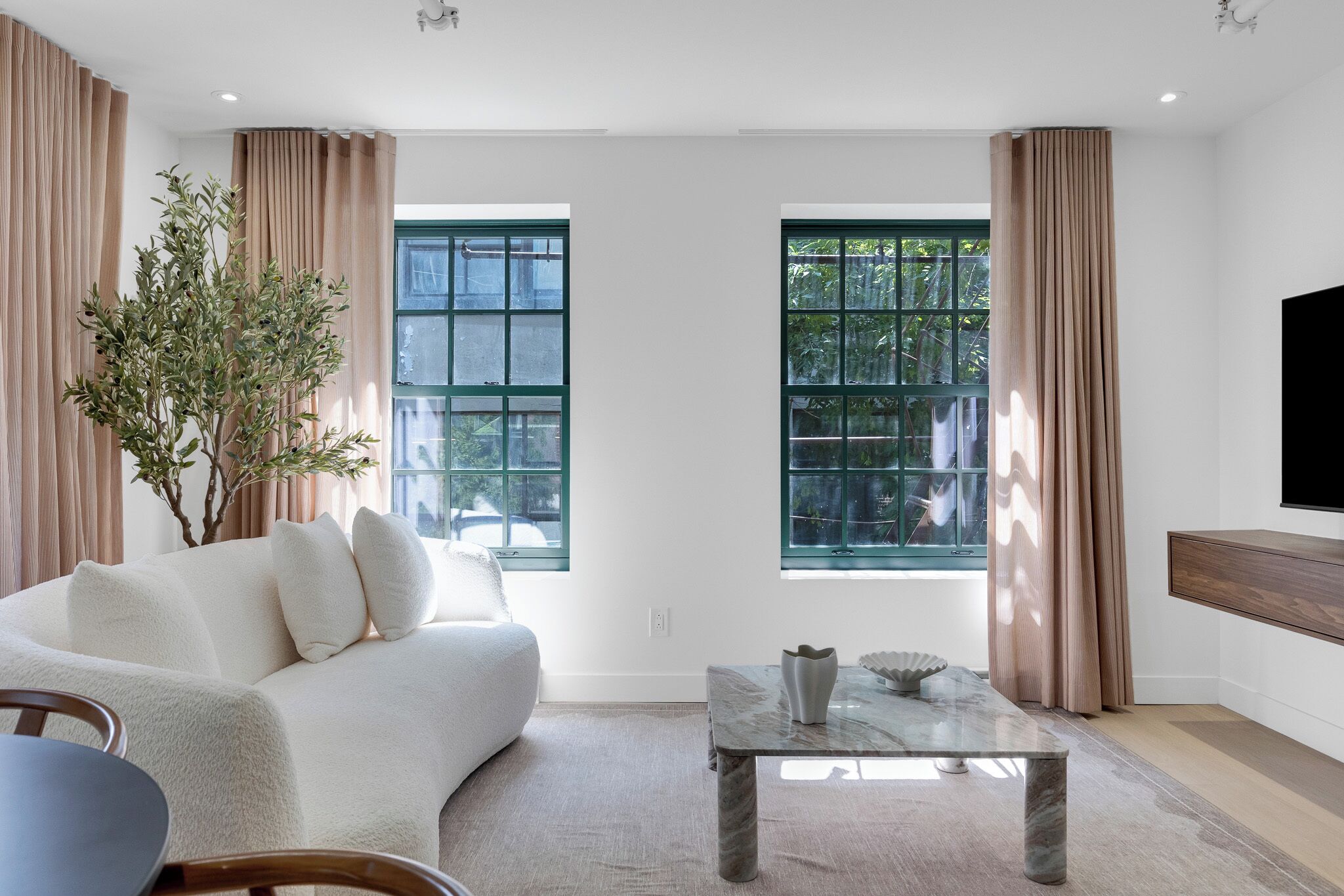 Uma sala de estar moderna com um sofá branco, uma mesa de centro de vidro e uma grande janela com cortinas.