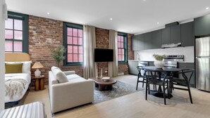 A modern living room with a sofa, a coffee table, and a TV. There is a kitchen area with cabinets and appliances. - The Mercer Boutique Hotel (Montréal)