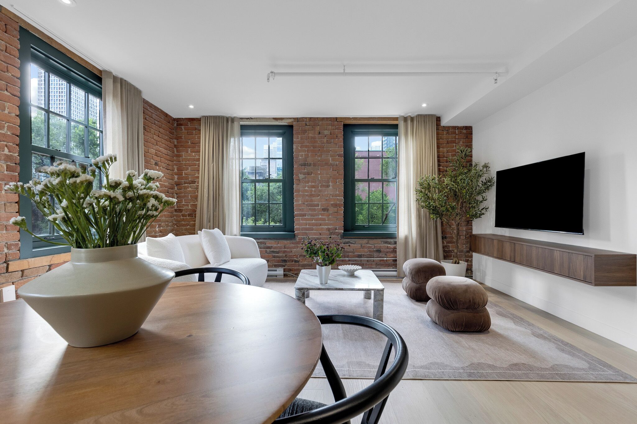 A modern living room with a brick wall, large windows, a flat-screen TV, and comfortable seating.