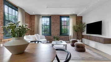A modern living room with a brick wall, large windows, a flat-screen TV, and comfortable seating.