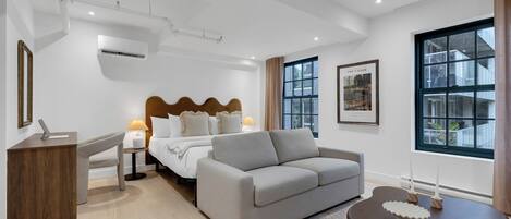 Ett modernt hotellrum med en säng, en soffa, ett skrivbord och ett fönster med utsikt över byggnader.
