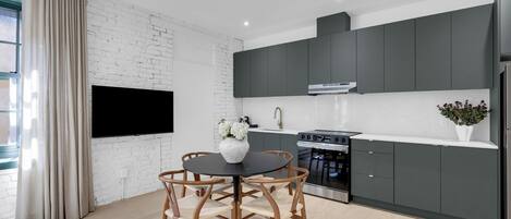 A modern kitchen with dark cabinets, a black dining table, and a flat-screen TV mounted on the wall.