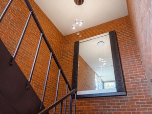 A staircase with metal railings, a large mirror reflecting a ceiling light fixture, and brick walls. - Galesburg Extended Stay I-74 (Newly Renovated) (Galesburg)