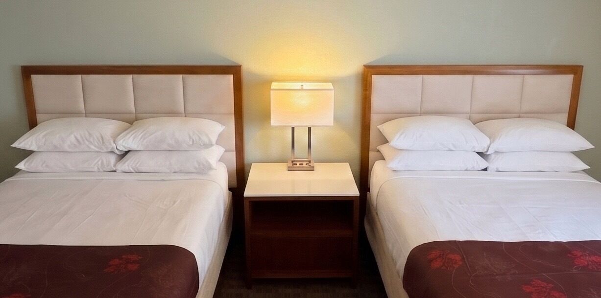A hotel room with two beds, a nightstand with a lamp, and a wooden headboard.