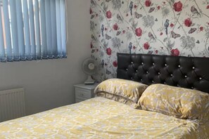 Un dormitorio con una cama, una mesita de noche, un ventilador y una ventana con persianas.