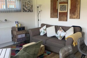 A living room with a grey sofa, floral cushions, a wooden side table, and a colorful rug.