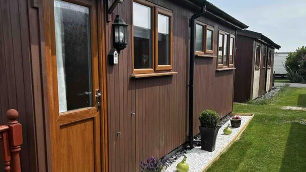 A row of wooden mobile homes with large windows and a gravel pathway with potted plants. - 2 Bed Chalet Sleeps 6 - Pets, Near Beach, Parking (Mablethorpe)