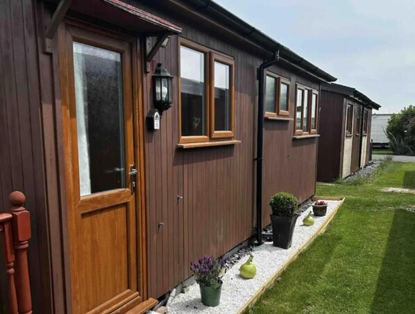 Una hilera de casas móviles de madera con ventanas amplias y un sendero de grava con plantas en macetas.