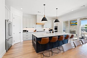 Een moderne keuken met witte kastjes, een centraal eiland met barkrukken, roestvrijstalen apparatuur en hanglampen.