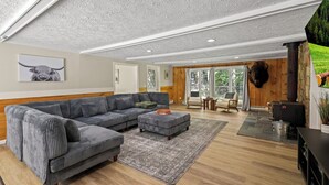 A spacious living room with a grey sectional sofa, a patterned rug, and a stone fireplace. - The Woodland Haven - Secluded 3 bed, 2 bath, and Hot Tub! (Great Valley)