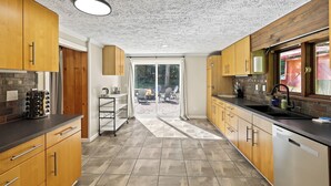 A modern kitchen with wooden cabinets, a black countertop, and a view to an outdoor patio area. - The Woodland Haven - Secluded 3 bed, 2 bath, and Hot Tub! (Great Valley)
