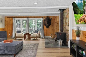 A cozy living room with a fireplace, wooden walls, and a mounted animal head. - The Woodland Haven - Secluded 3 bed, 2 bath, and Hot Tub! (Great Valley)