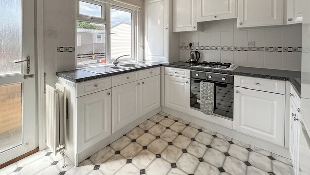 A kitchen with white cabinets, a black countertop, and a patterned floor. - 1 bedroom accommodation in Newton Stewart (Newton Stewart)