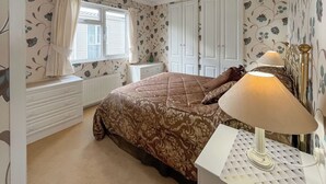 A bedroom with a bed, a bedside table with a lamp, a window with curtains, and a radiator. - 1 bedroom accommodation in Newton Stewart (Newton Stewart)