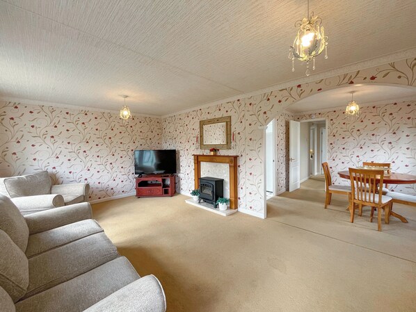 A living room with a fireplace, a television, and a dining area with chairs.