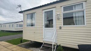 A mobile home with a front door, a small porch, and a window with curtains. - Marine Getaways Caravan Hire

A home from home experience in luxury.. (Rhyl)