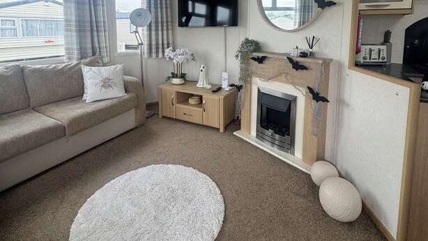 A living room with a sofa, a round mirror, a fireplace, and a television. - Marine Getaways Caravan Hire

A home from home experience in luxury.. (Rhyl)