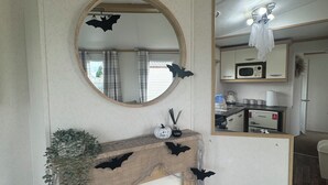 A living room with a fireplace, a round mirror, and Halloween decorations. - Marine Getaways Caravan Hire

A home from home experience in luxury.. (Rhyl)