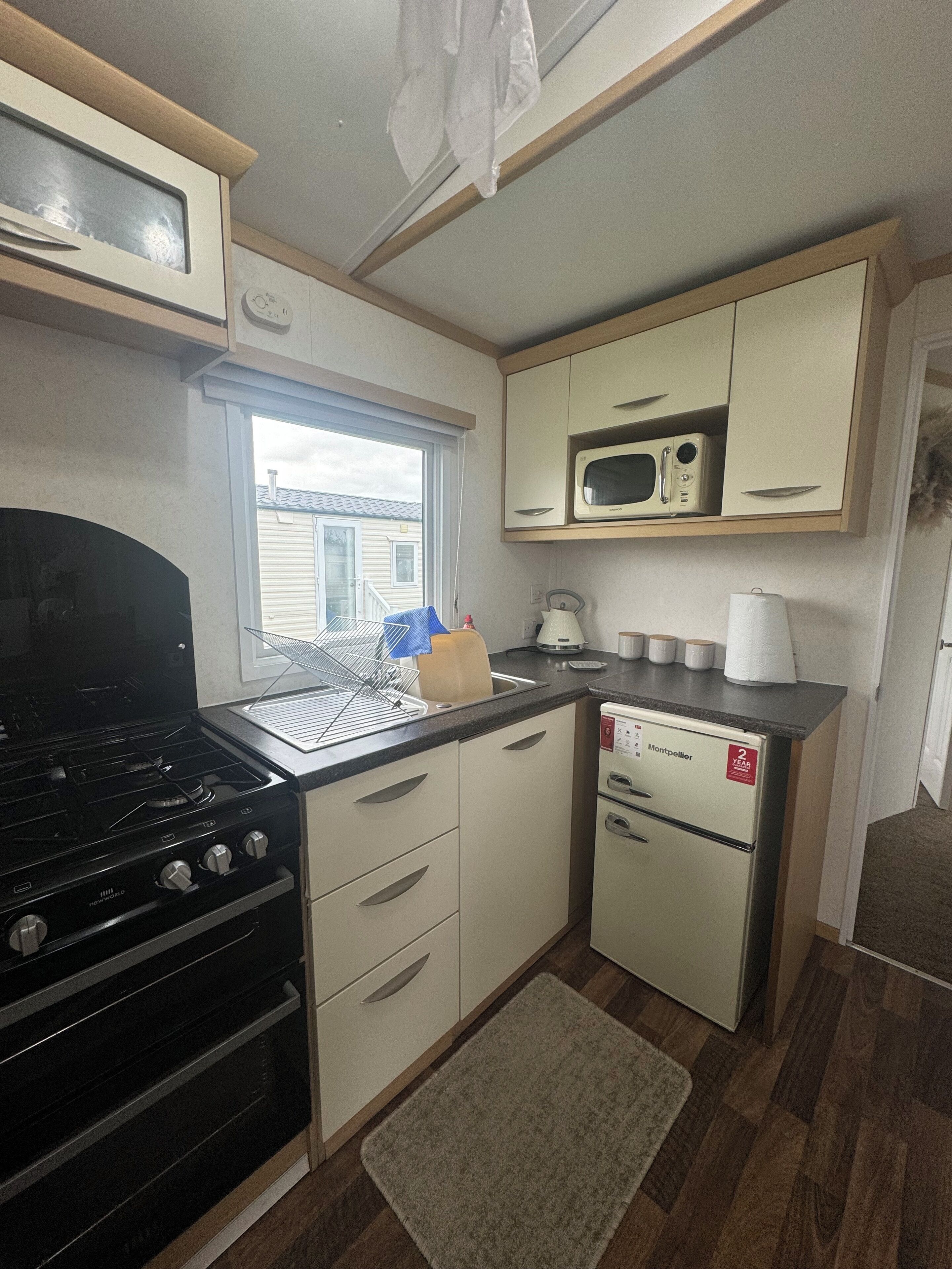 Cocina compacta con estufa, microondas, refrigerador y ventana con vista a un barrio residencial.