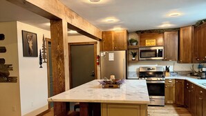 Una cucina moderna con mobili in legno, un'isola centrale con sgabelli da bar, un frigorifero in acciaio inossidabile e un forno a microonde.