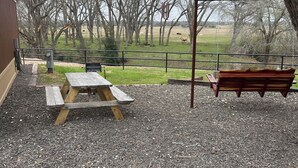 A picnic area with a wooden table and benches, surrounded by gravel and trees. - Cabin Unit 3 of 6 Called the Texan with WiFi and AC in serene Paige (Paige)