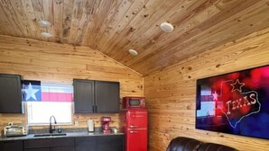 A cozy cabin interior with a wooden ceiling, a kitchenette, a leather sofa, and a Texas-themed wall decoration. - Cabin Unit 3 of 6 Called the Texan with WiFi and AC in serene Paige (Paige)