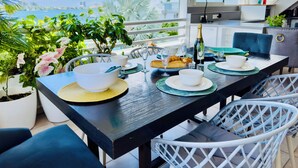 Un coin repas avec vue sur la mer, une table dressée avec des assiettes, des verres et une bouteille de champagne.