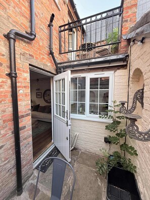 Ein Backsteinhaus mit einer weißen Tür, einem Balkon mit Metallgeländer und einem Blumentopf.