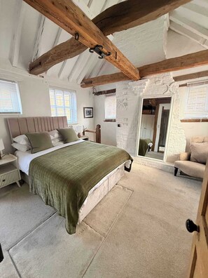 Ein Schlafzimmer mit Bett, Nachttisch, Kommode, Spiegel und einer Tür zu einem anderen Raum.