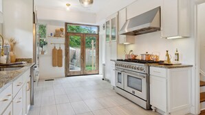 A spacious kitchen with white cabinetry, a large island with a stove, and a view to the outdoors through a glass door.