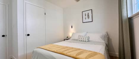 A bedroom with a bed, a ceiling fan, a nightstand, a framed picture on the wall, and a window with curtains.