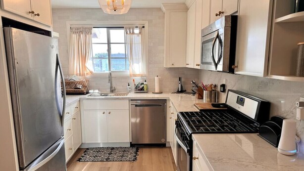 A modern kitchen with stainless steel appliances, white cabinetry, and a window providing natural light.