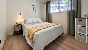 A bedroom with a bed, a nightstand, a ceiling fan, a window with curtains, and a storage unit.