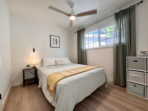A bedroom with a bed, a nightstand, a ceiling fan, a window with curtains, and a storage unit. - 4 Bed 2 Bath House Near Everything in San Diego.  (San Diego)