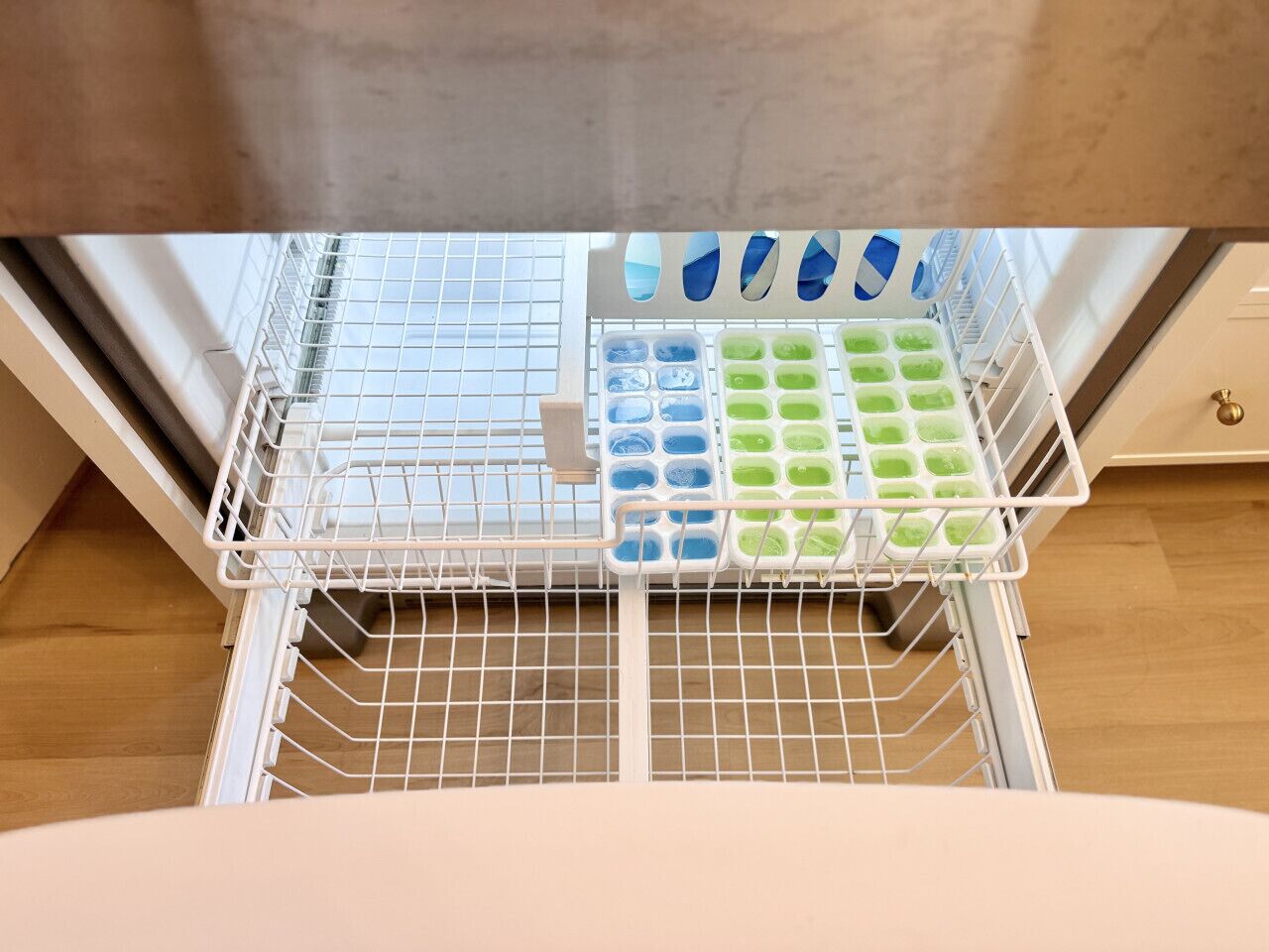 A kitchen with a white wire rack holding ice cubes in blue and green containers.