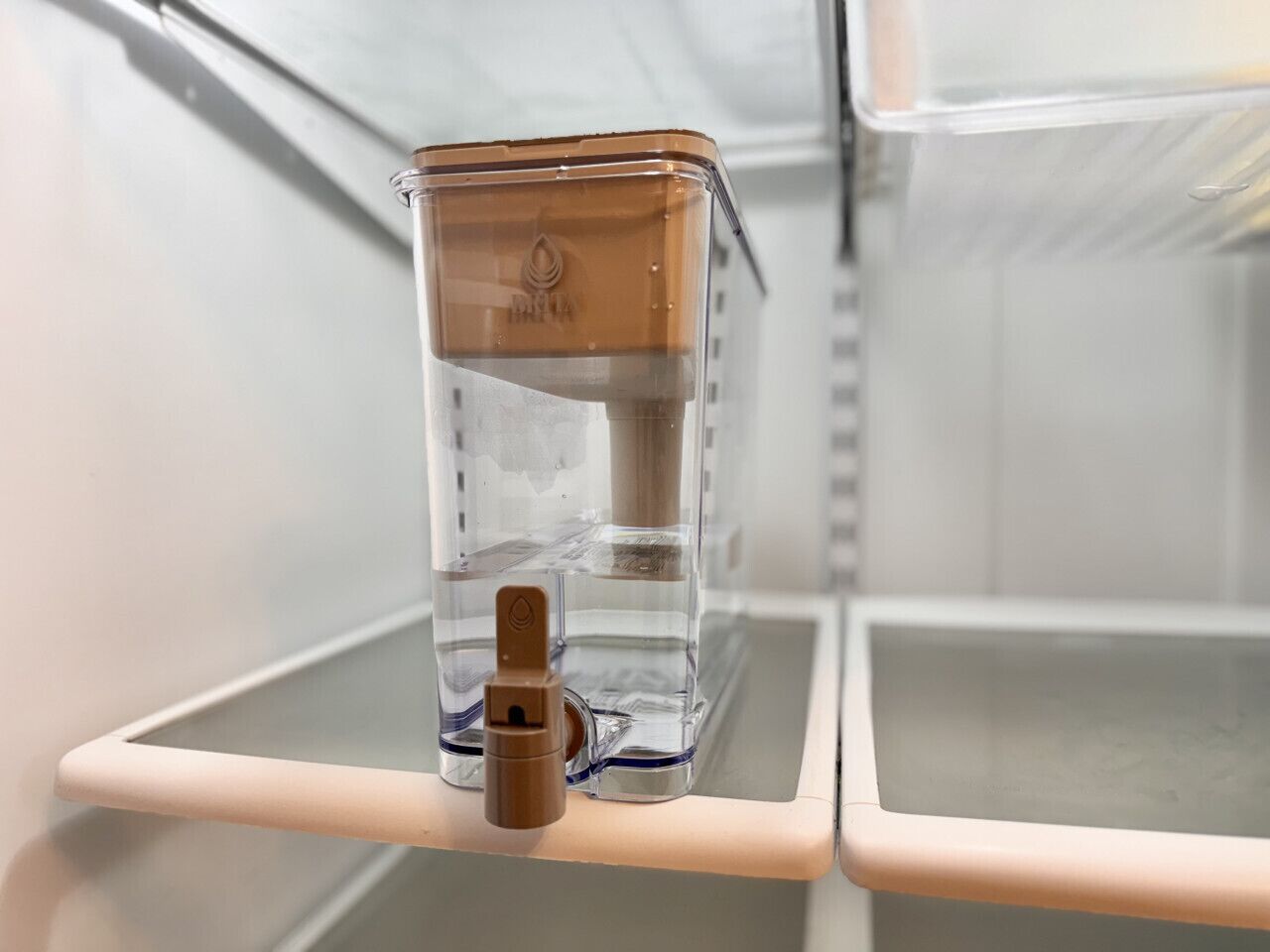 A clear water dispenser on a white shelf in a room.