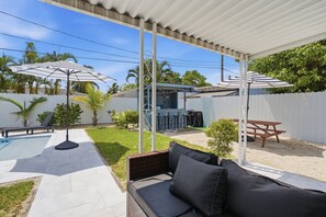 Un patio techado al aire libre con piscina, sillones de descanso y sombrillas.