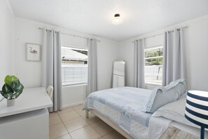 Un dormitorio con cama, escritorio, silla, planta y ventana con persianas.