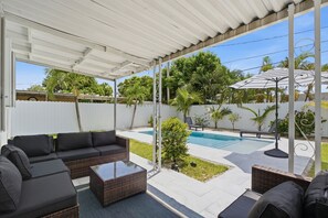 Un patio techado al aire libre con piscina, mobiliario de sala de estar y vista al jardín.