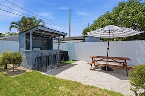 Ein Garten mit Grillplatz, Picknicktisch und weißem Zaun.