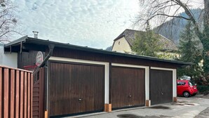 Un edificio con tres grandes puertas de garaje de madera, un coche rojo estacionado al frente y montañas al fondo.