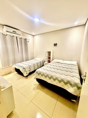 A room with two beds, a small desk, an air conditioning unit, and a shelf with a few items. - Residence with swimming pool and barbecue, very large and cozy house (Pricumã Boa Vista)