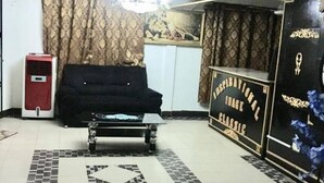 A living room with a sofa, a coffee table, a red air cooler, a patterned curtain, a wall-mounted sign, and a tiled floor. - Image Classic Hotel (Kwabenya)