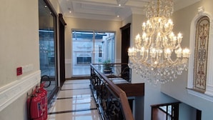 A grand hallway with a chandelier, a fire extinguisher, and a view of a building through glass doors. - Spanish Villa/5 BHK/Raya Golf course & Cinema 2Kms (Lahore)
