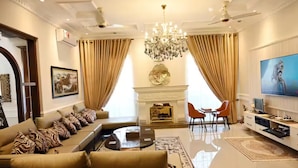 A spacious living room with a sofa set, a fireplace, a chandelier, and a television. - Spanish Villa/5 BHK/Raya Golf course & Cinema 2Kms (Lahore)