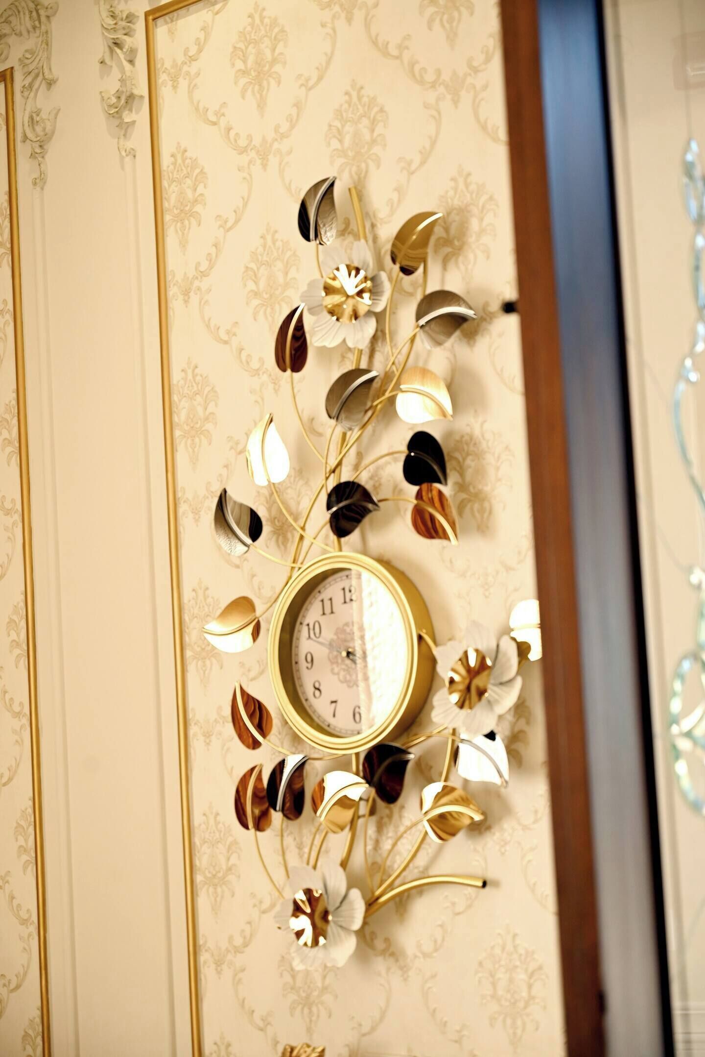 Eine Wanduhr mit floralem Dekor, vor einem Wandpapier mit Goldmuster.