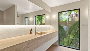 Enjoy a serene atmosphere in this stylish bathroom with a large mirror, single sink, and lush greenery view.