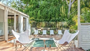 Relax in a serene outdoor space with a glass-enclosed pool surrounded by lush greenery and comfortable lounge seating.
