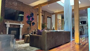 A spacious living area with a brick fireplace, a large sectional sofa, and a wooden floor. - 3-Bedroom, Outdoor Japanese Soaking Tub, Fire-Pit, originally built in 1890!   (Denver)